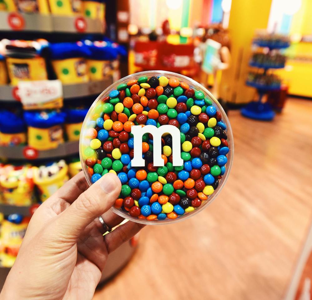 hand holding bowl of m&m candies, white "m"